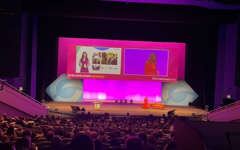 Rachael Flanagan, wearing a red suit, addresses the Entrepreneurs Circle: Getting and Keeping Customers Convention 2022 as a headline speaker