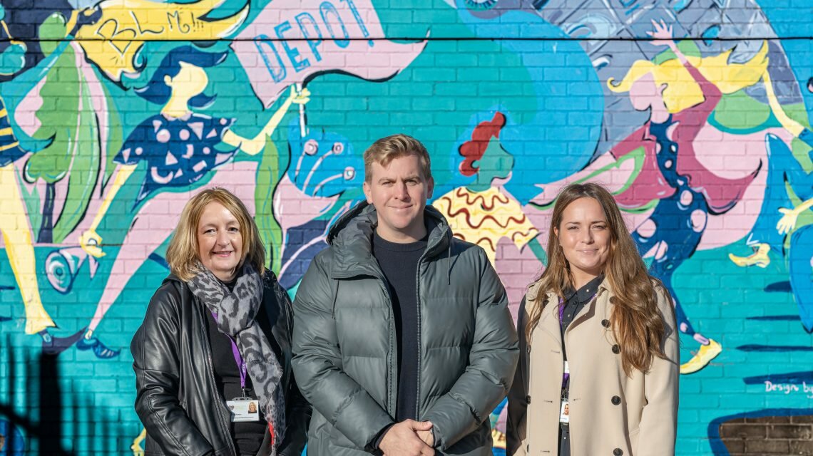 Amanda Fenton, Nick Saunders, Daisy Magill stand in front of a colourful wall