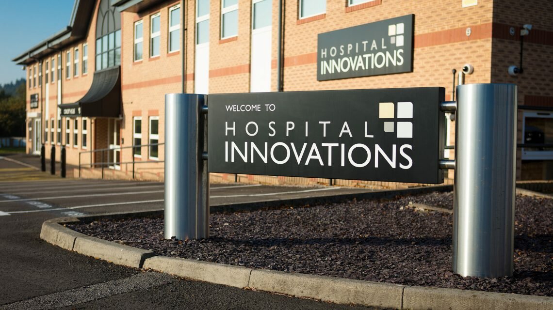 A black welcome sign with white writing and the Hospital Innovations logo stands outside their Talbot Green headquarters