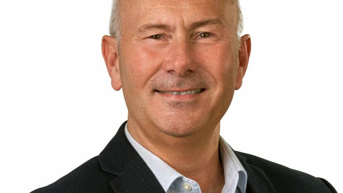 Peter Kinsey smiles. He is wearing a light shirt and dark blazer.