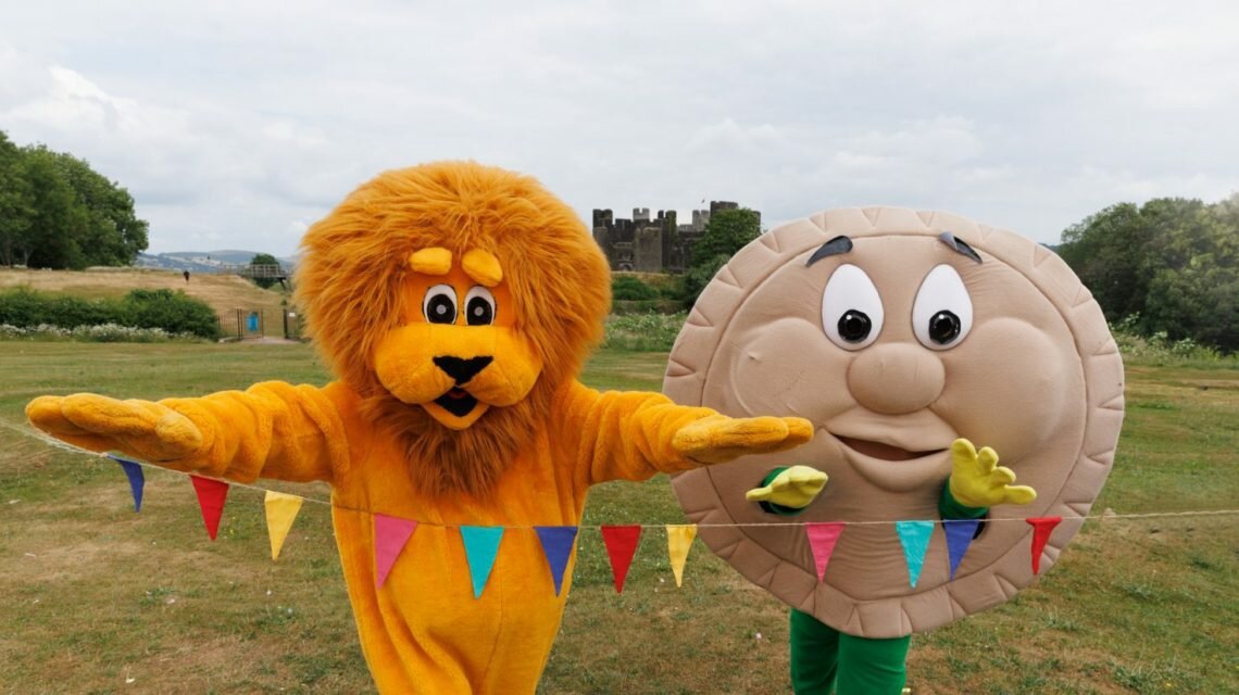 A lion mascot and pie mascot run towards a multicoloured bunting finish line. In the background is Caerphilly Castle.
